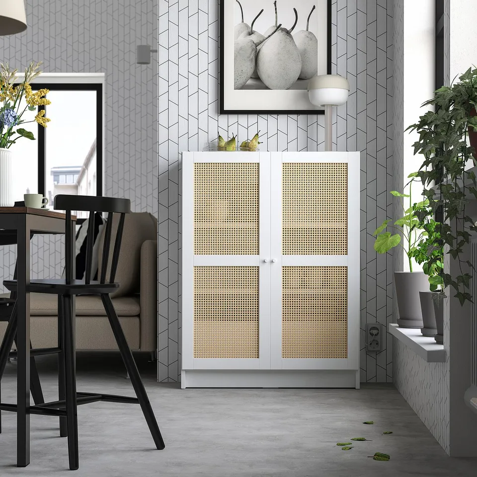 Modern living space with white and grey decor, featuring a BILLY bookcase with bamboo doors, a grey sofa, black chairs, and a stylish plant.