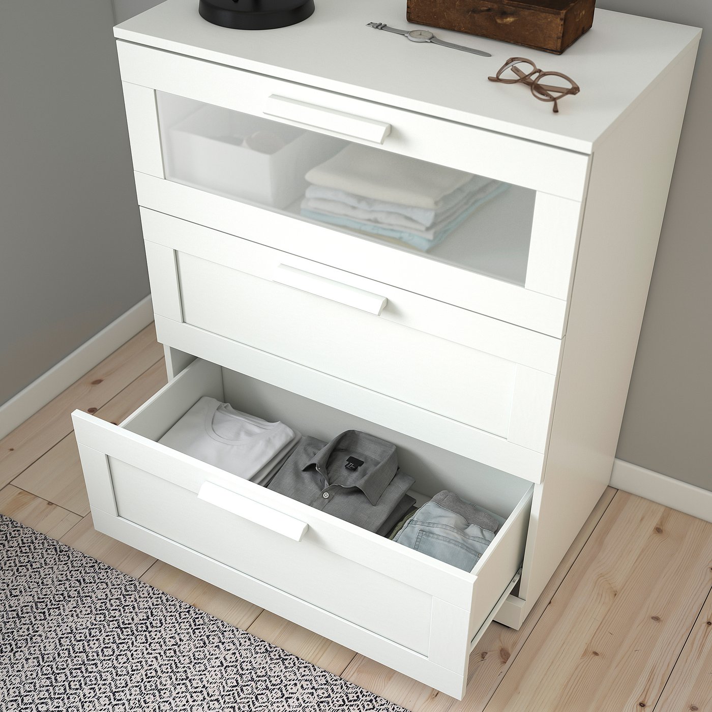 White chest of drawers with three drawers. Open drawer reveals folded clothes. Frosted glass top drawer. Safe & stable design.