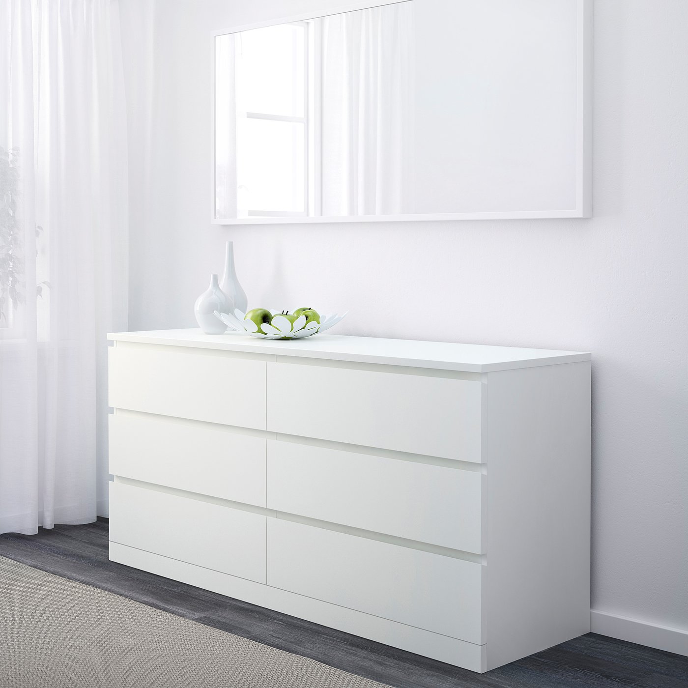 A white MALM chest with 6 drawers. A decorative bowl and apples sit on top. Its positioned under a large mirror.