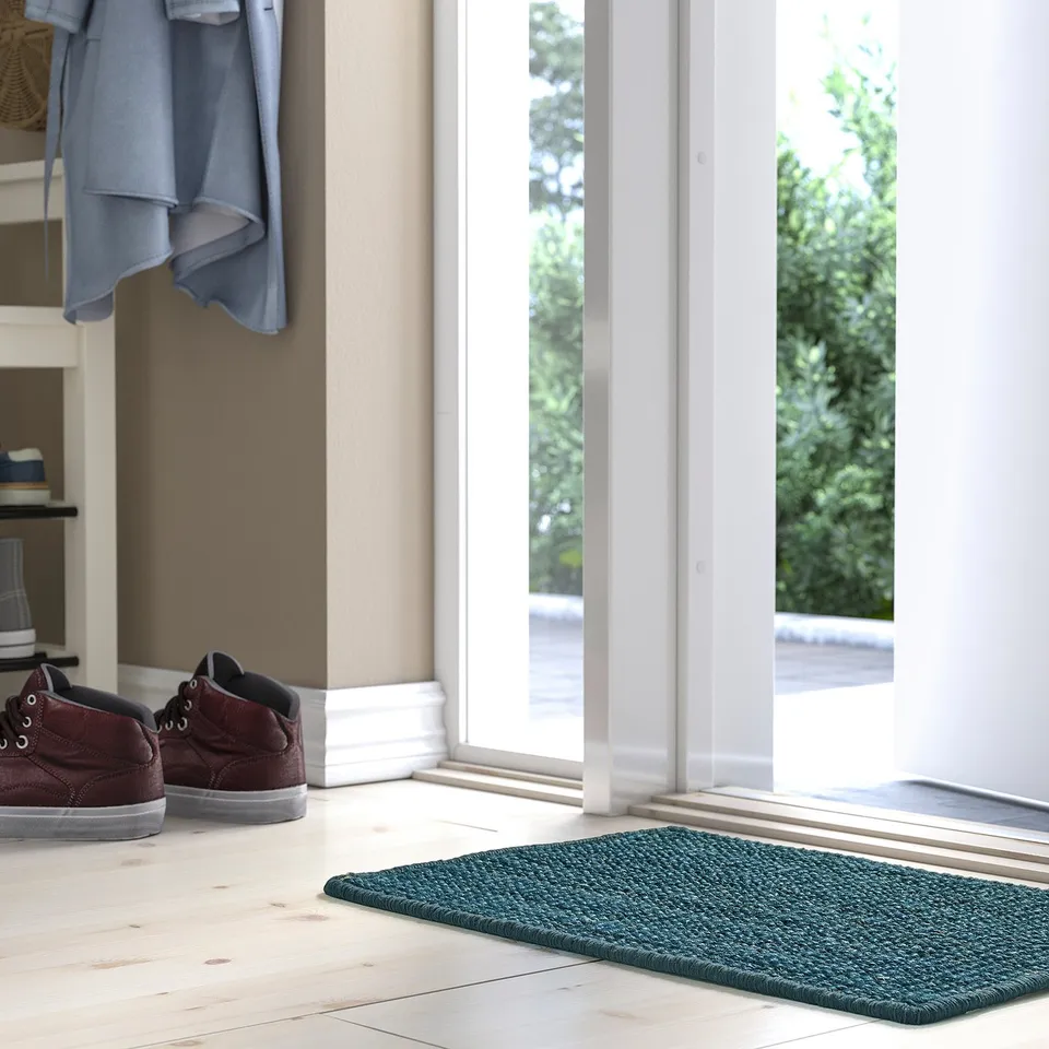 Entryway scene with LANDBANA dark blue jute mat, red trainers, and hanging blue garment, leading to bright outdoor view.