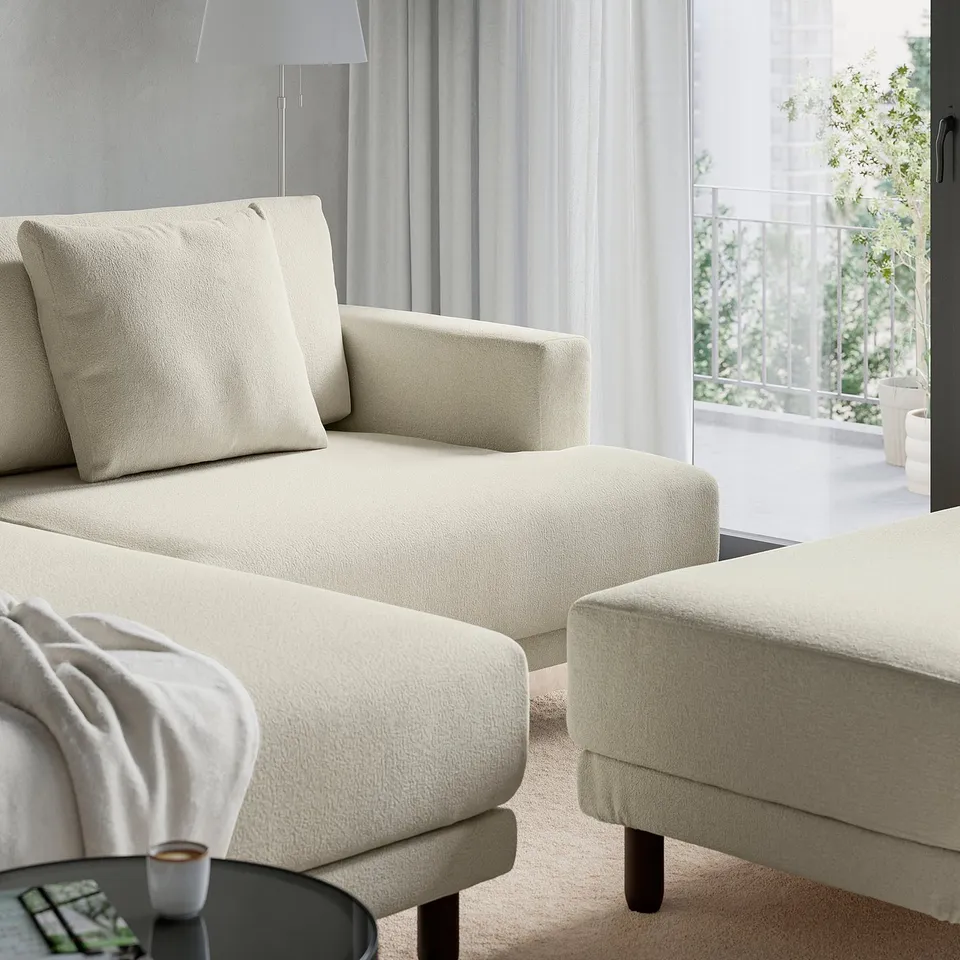 A modern living room a light-colored UPPÅKRA sofa with large cushions designed for comfort. Atable with coffee sits nearby, and a lamp stands behind.