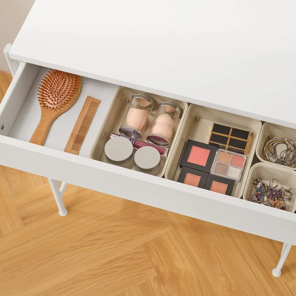 White dressing table drawer open, showing organised compartments with makeup brushes, makeup palettes, and jewellery.