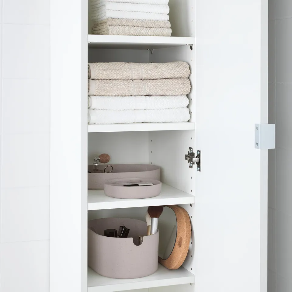 White cabinet with folded towels and three jars for toiletries, including tweezers and brushes.