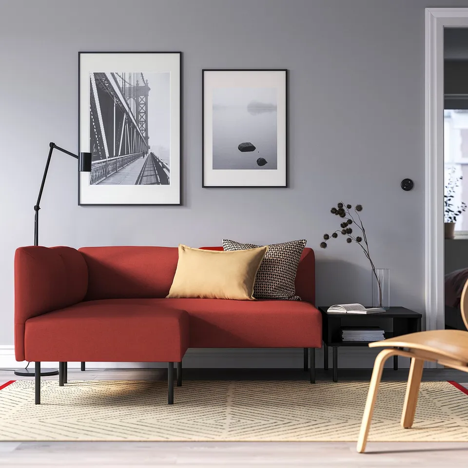 Modern living room with red LILLEHEM sofa, yellow/black/white cushions, bridge/abstract art, black side table, and beige rug.