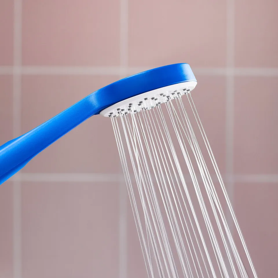 Blue shower head pouring water against pink tiled wall.