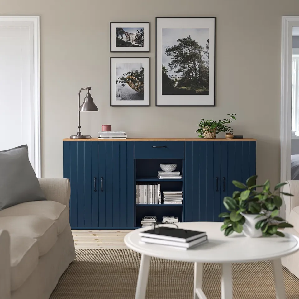 Cosy living space with blue SKRUVBY cabinet, white lamp, framed photos, and round table with green plant.