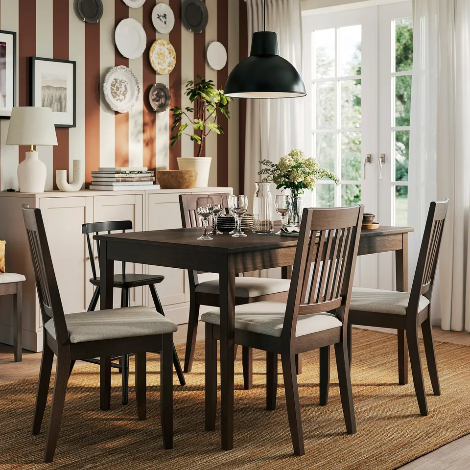 A cosy dining nook with a dark wood table, beige cushions, striped rug, and plate wall, illuminated by a large window.