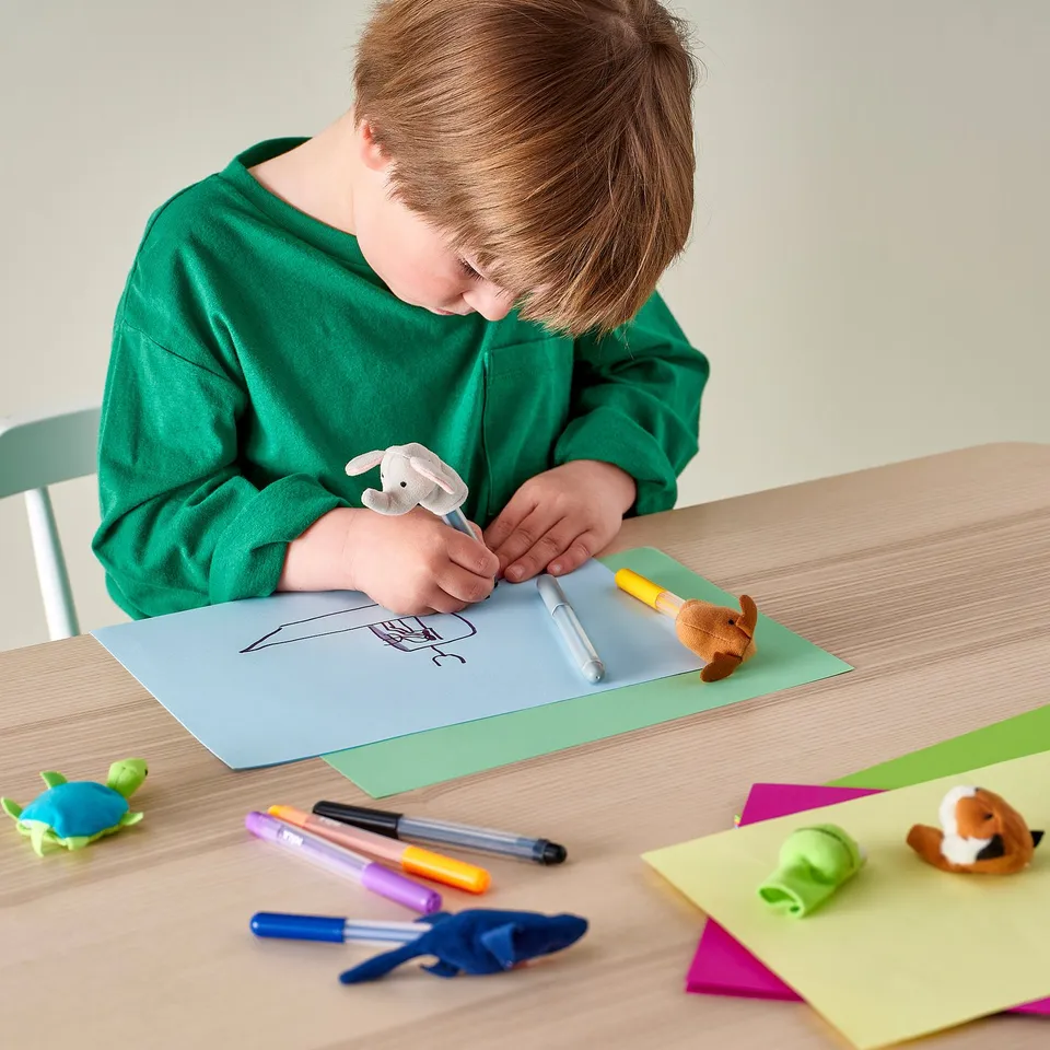 Child colouring with yellow marker, surrounded by papers and finger puppets.