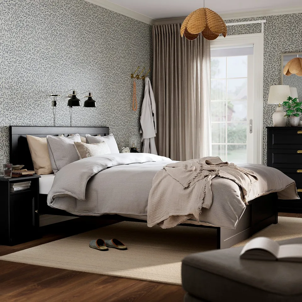 Black oak FÅGELFJÄLLET bedroom: bed, bedside tables, rug, white linens, striped duvet, decorative wallpaper, curtains, slipper, chair, pendant lamps.