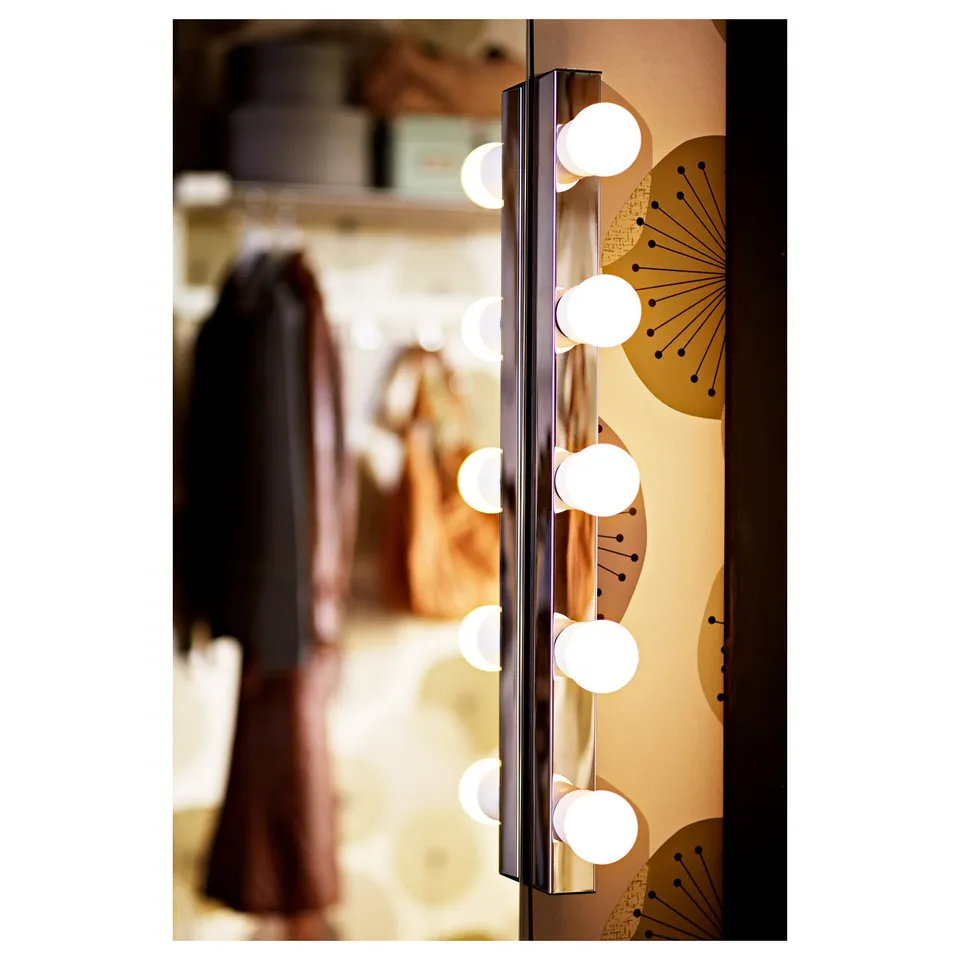Vertical wall lamp with lit globes beside mirror in hallway.