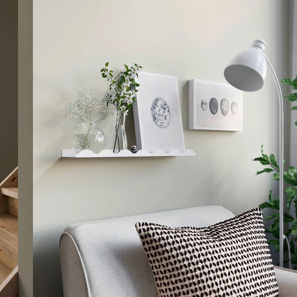 Shelf with vases, flowers, art. Grey sofa, patterned pillow, white lamp.