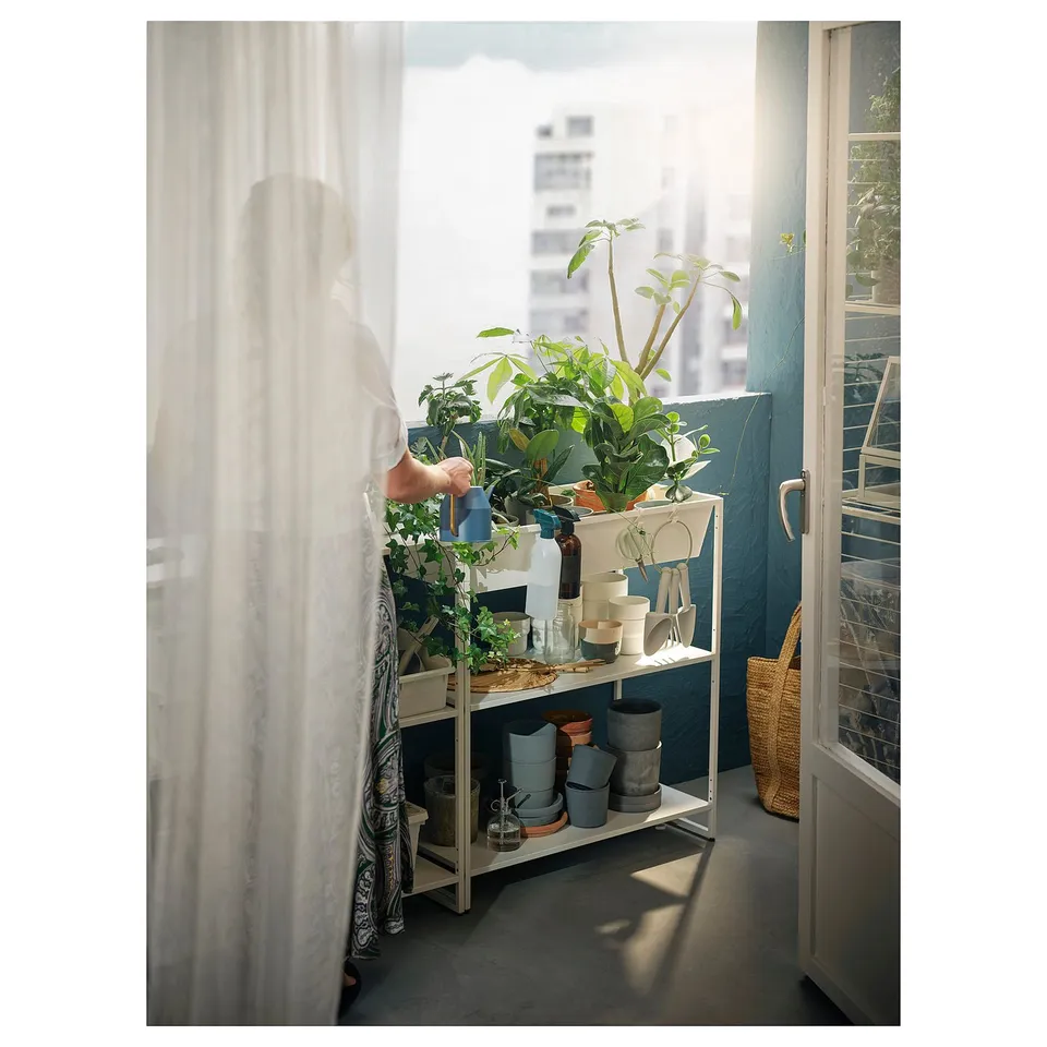 Person waters indoor plants on JOSTEIN shelf near window.
