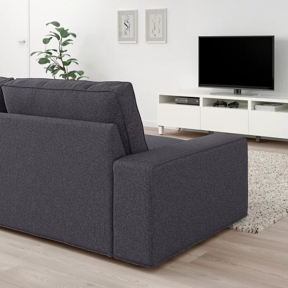 Modern living room featuring large grey KIVIK sofa, flat-screen tv on stand, white decor, and plant.