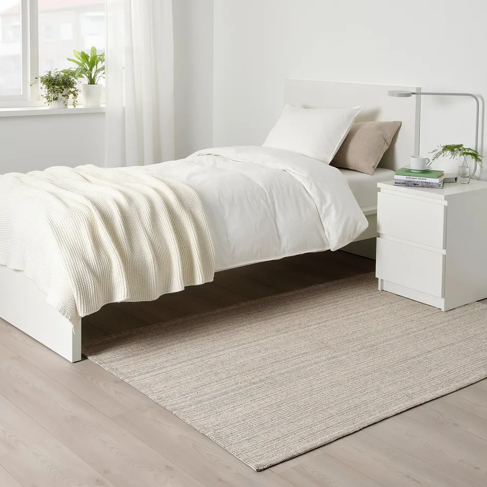 Minimalist bedroom with white TIPHEDE rug, white bed, bedside table & lamp. Rug is cotton, fits perfectly under bed.