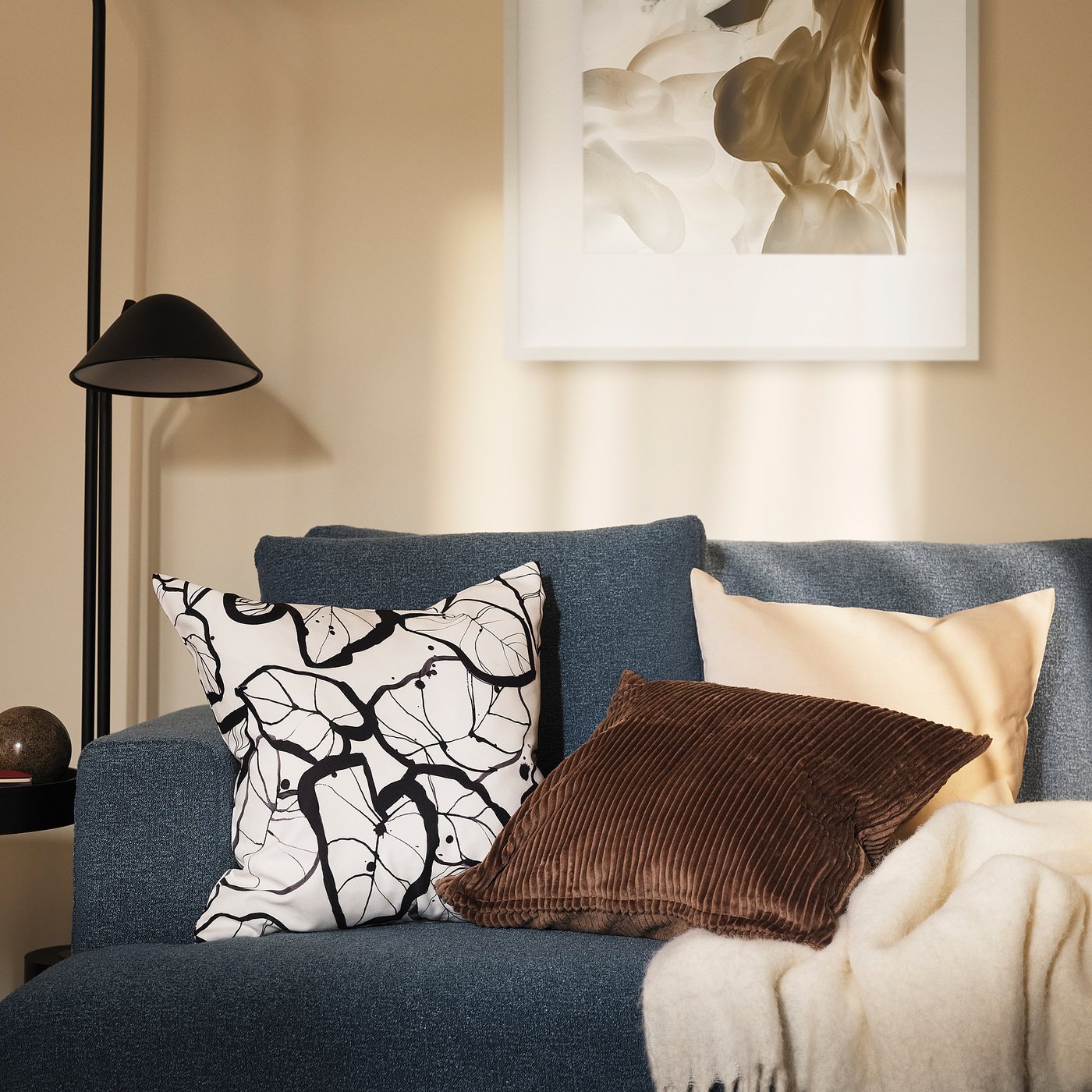 Stylish PELARKÖRSBÄR black-white leaf cushion on blue sofa, 100% recycled polyester.
