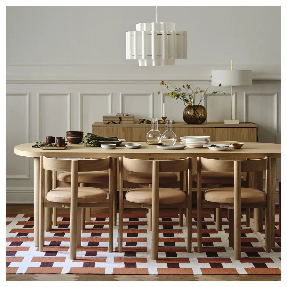 Modern dining set with light oak table and chairs, unique moon-shaped design, under stylish pendant light. Vibrant patterned rug adds warmth.