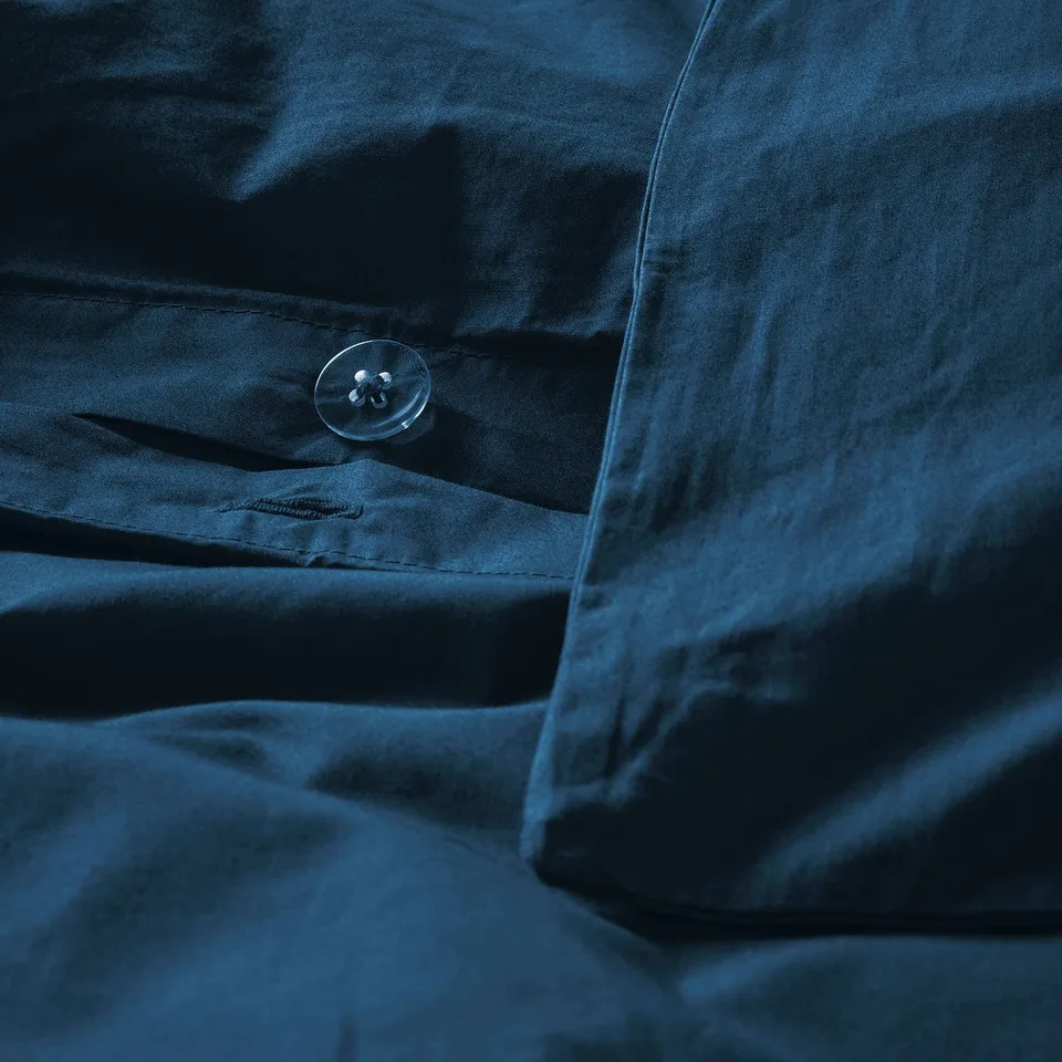 A close-up of a dark blue duvet cover with intricate stitching and a visible button for secure closure, highlighting its crisp cotton percale weave.