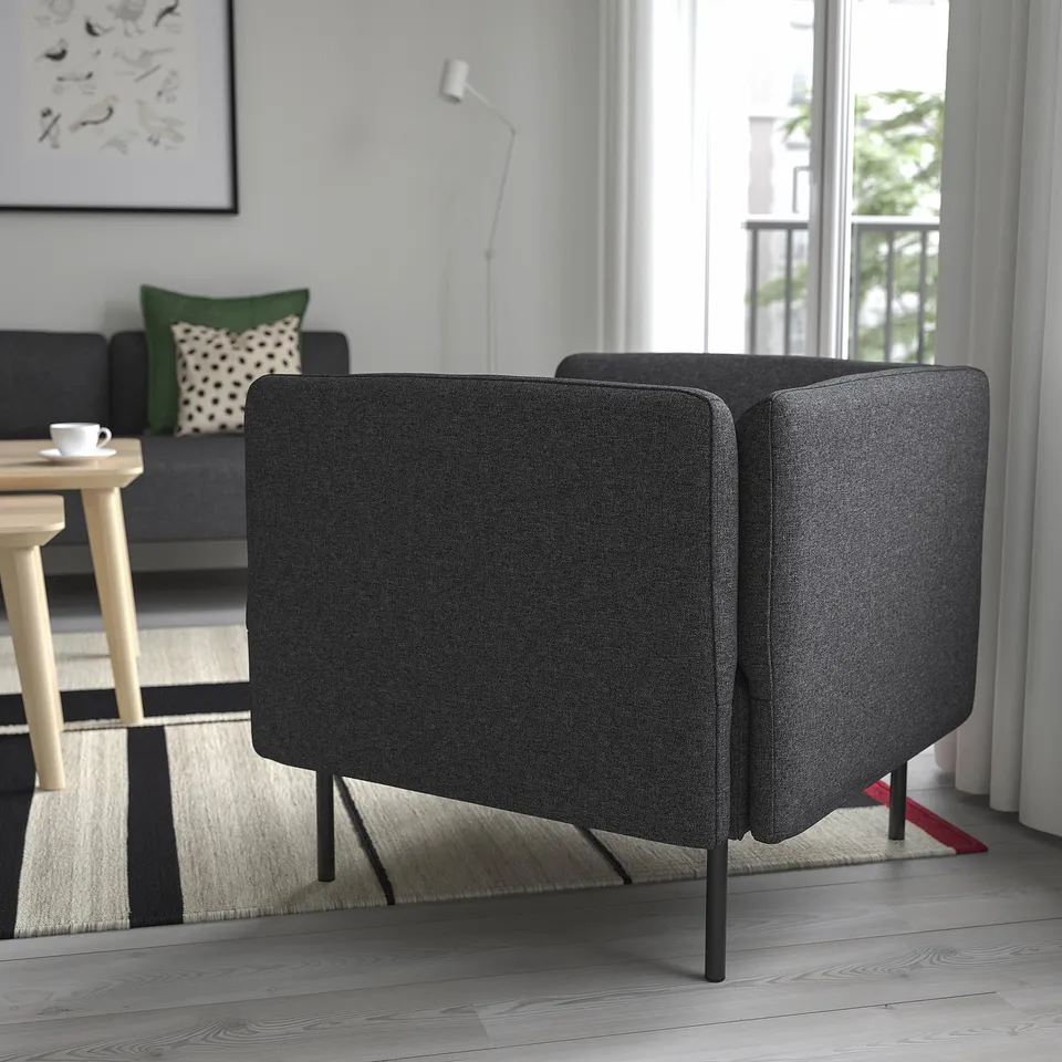 Modern living room with convertible sofa, grey upholstery, black/white rug, wooden side table, and daylight.