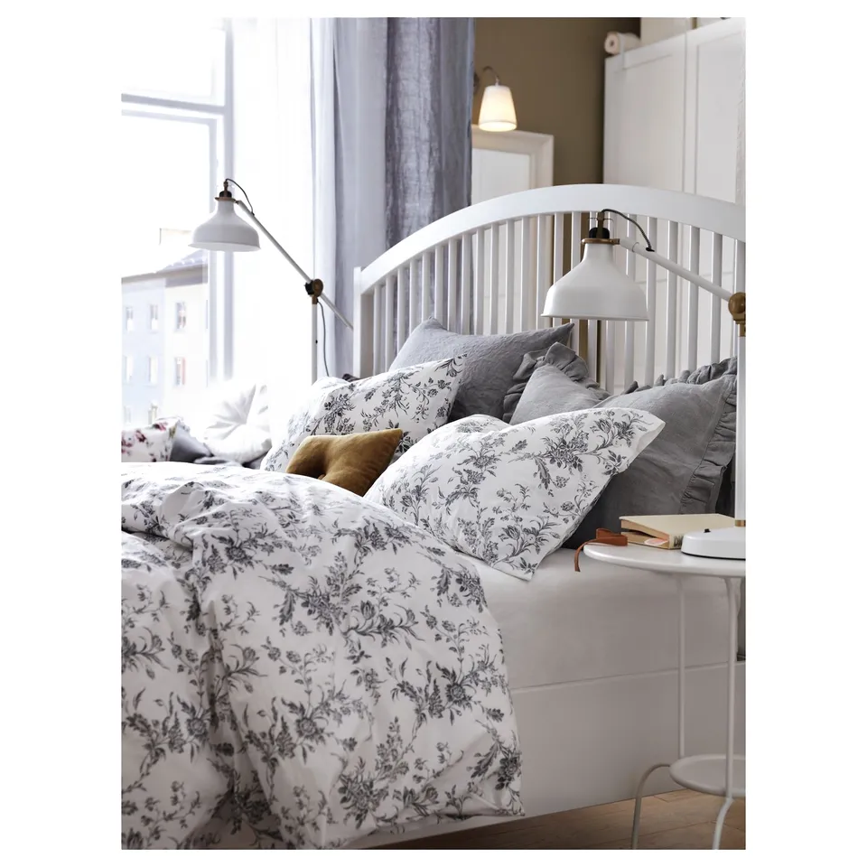 Cosy bedroom with wooden bed, grey bedding, wall lamps, and book on bedside table.