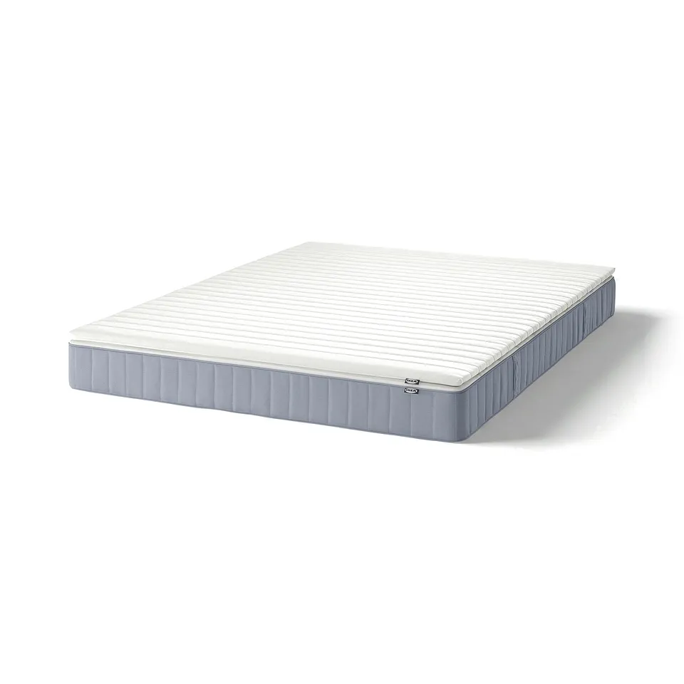 A white VESTERÖY mattress with a blue underside on a plain background. Its rectangular and vertical seams.