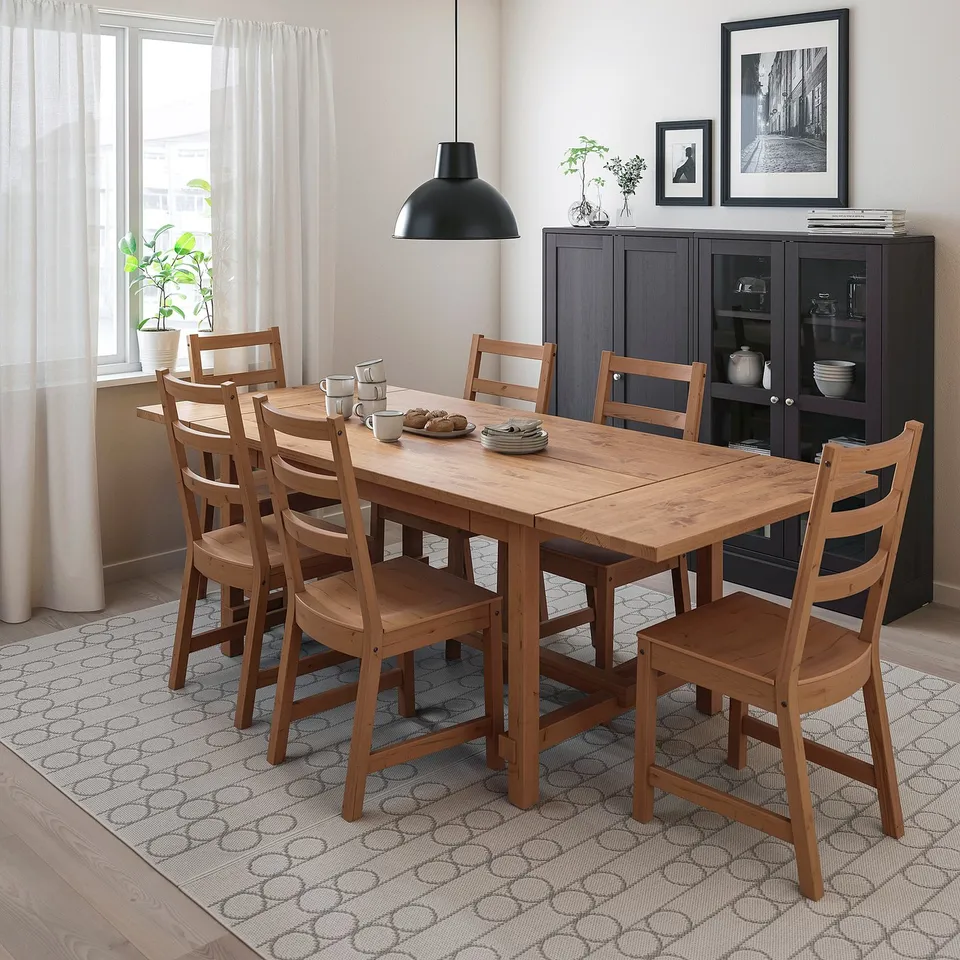 Modern dining room with NORDVIKEN table, chairs, and patterned rug. Black pendant light, dark sideboard, and sheer curtains.
