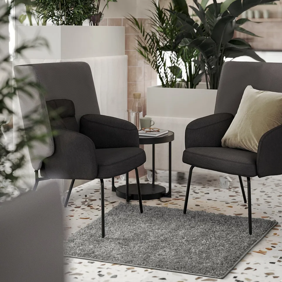 Grey armchairs, rug, table with mug, vase, snacks, green plants.