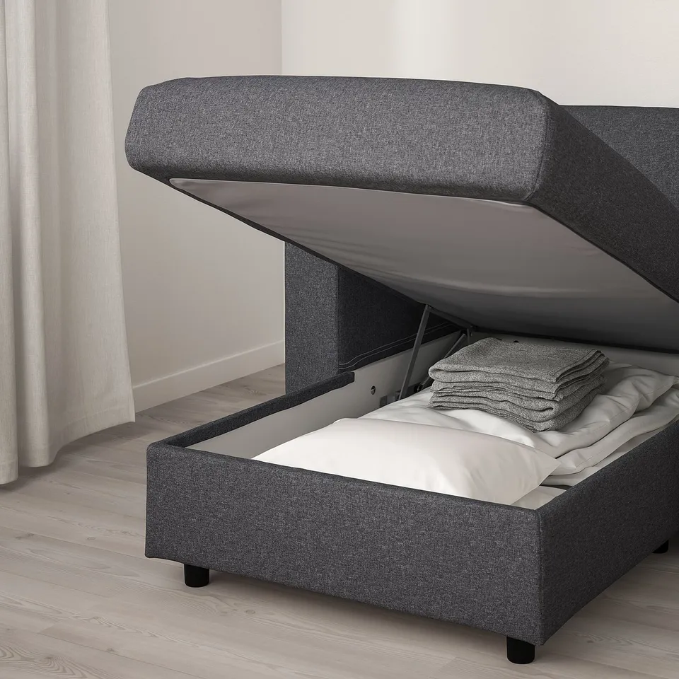 Grey upholstered bed with storage, headrest, and angled lid.