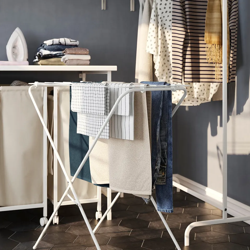 Foldable drying rack holding clothes, part of laundry setup.