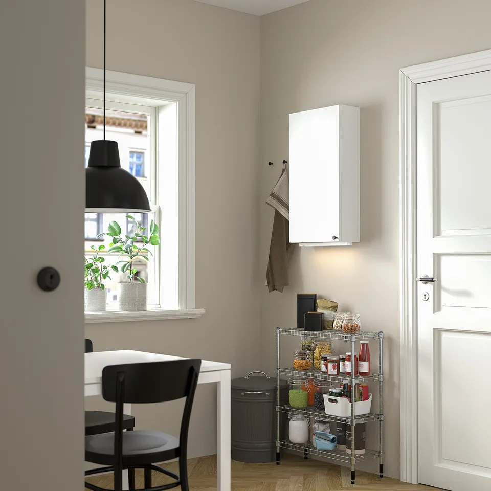 Small kitchen corner with white OMAR cabinet, black chair, and metal spice rack. White door, black lamp, and potted plant by window.