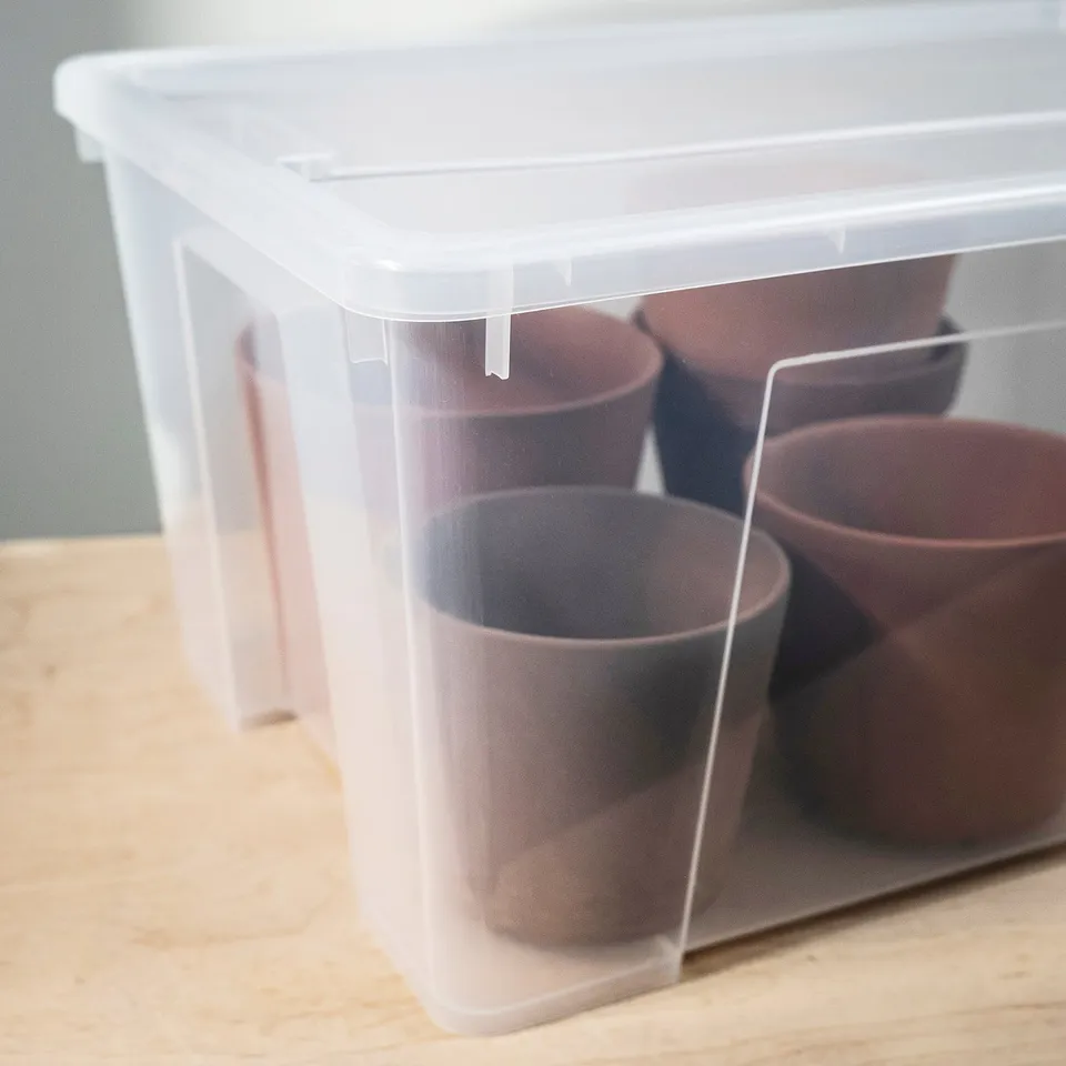 Clear plastic storage box with lid, containing four brown cups, neatly stacked on a wooden surface.