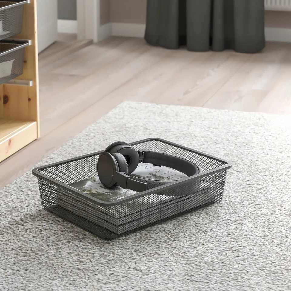 Mesh storage bin on carpet, holding headphones and a cd case, perfect for organising small items.
