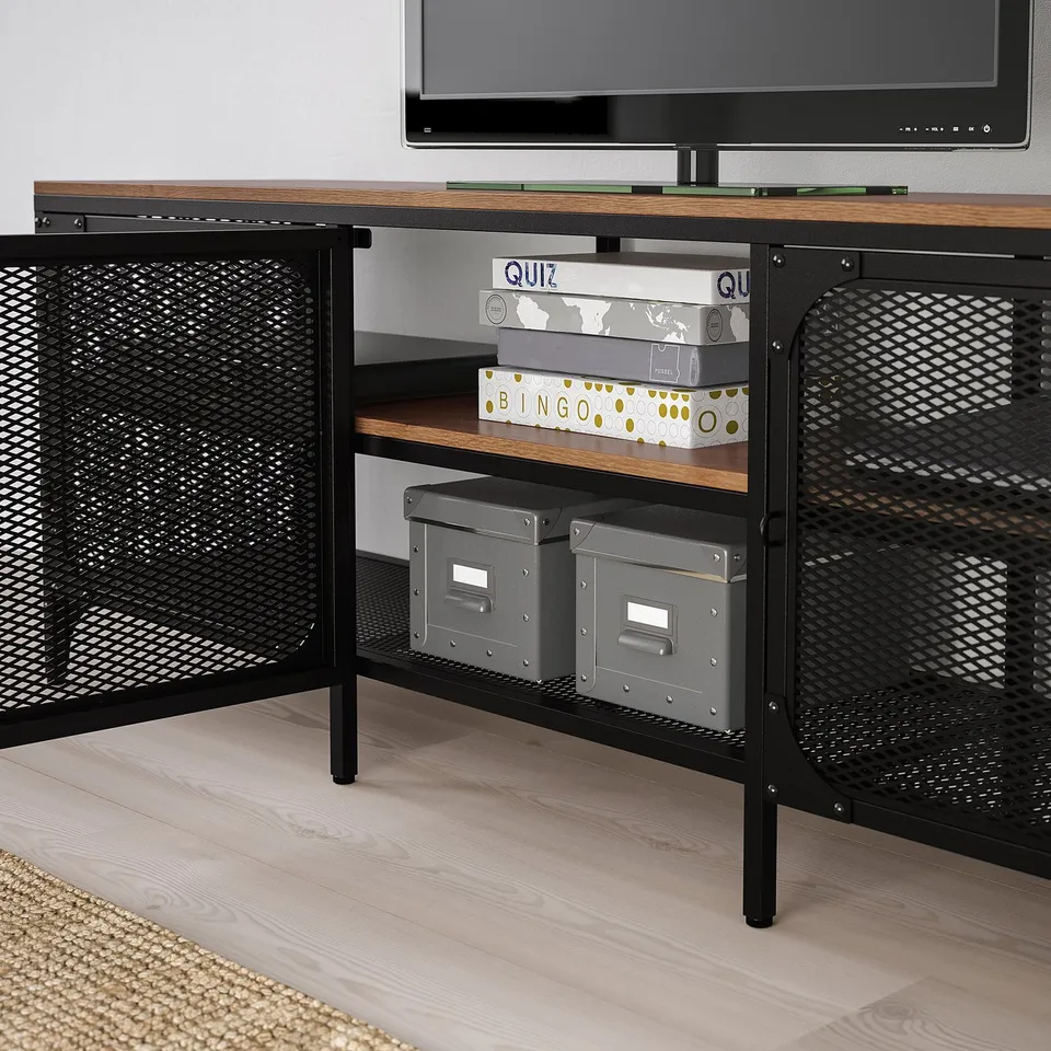 A wooden tv stand with mesh doors, housing board games and storage bins beneath the screen.
