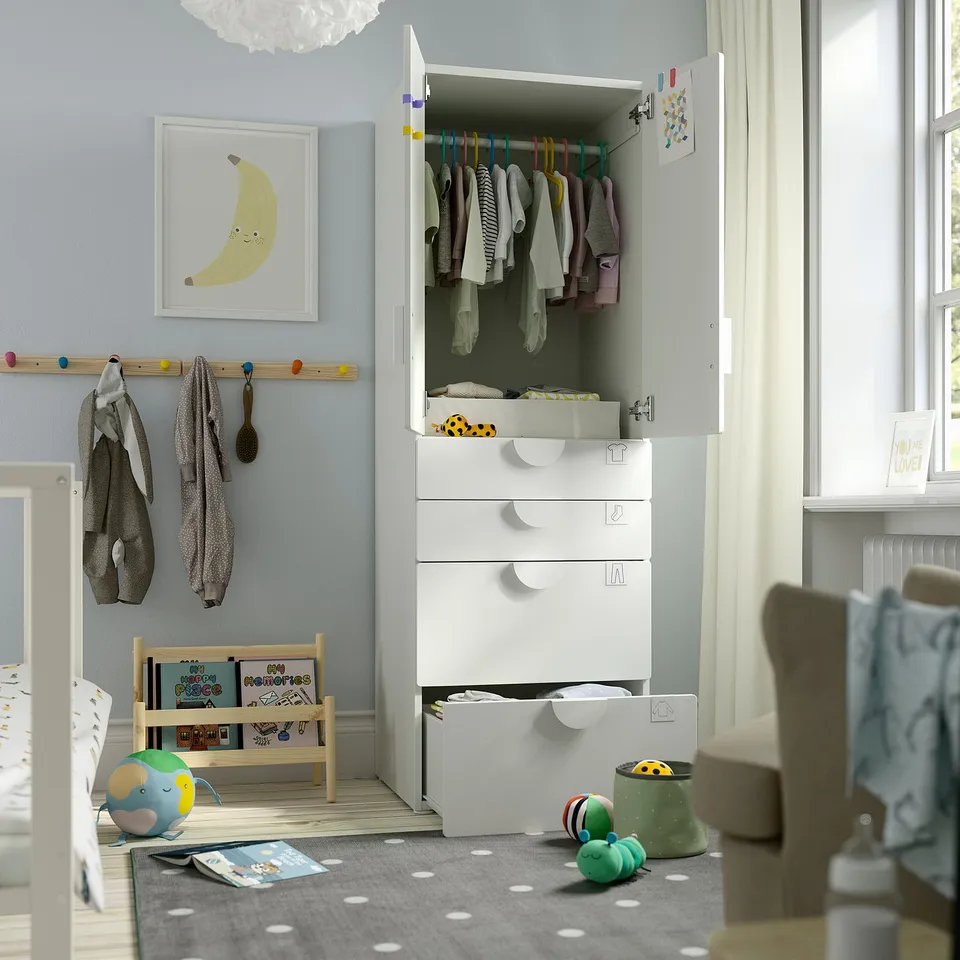 Baby room with white wardrobe, clothes, changing station, toys, books, and art.