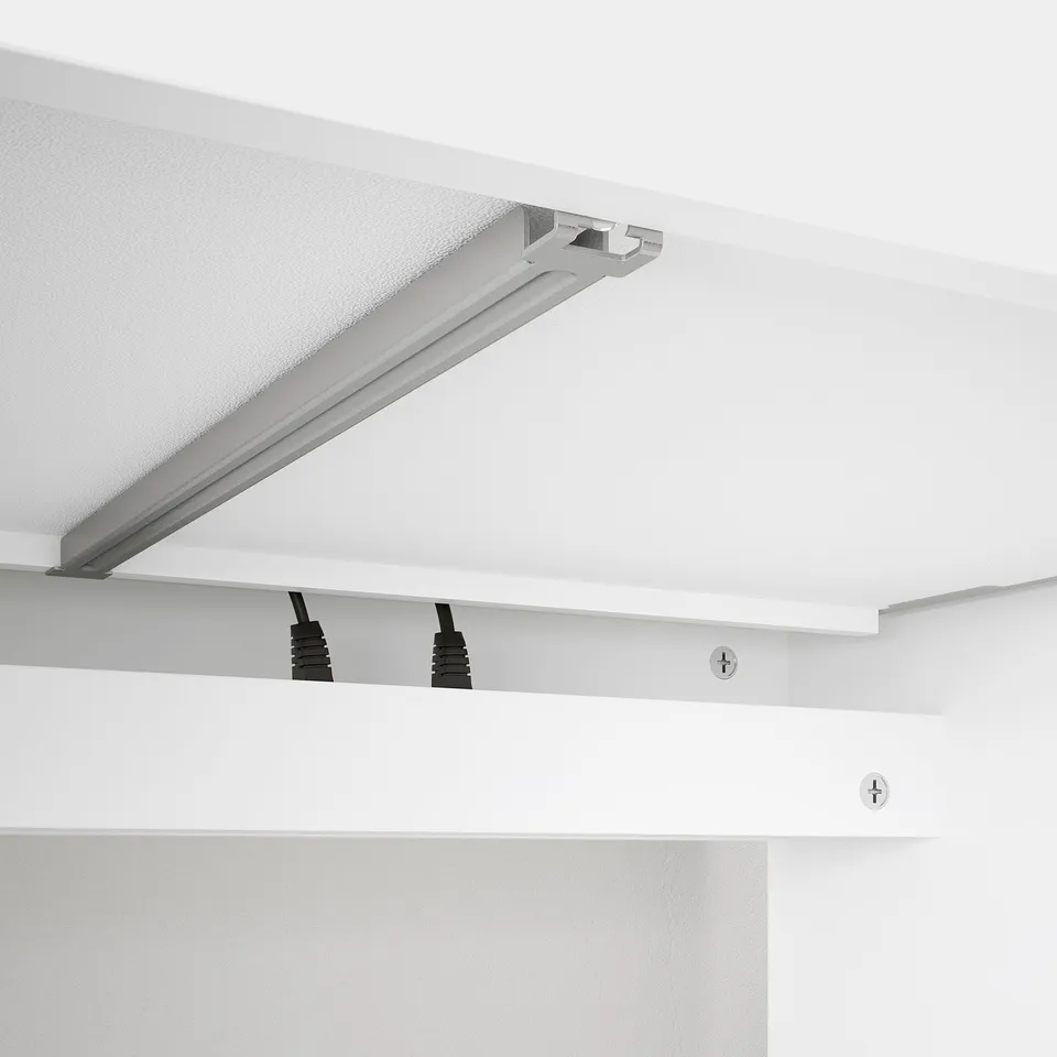 Desk with cable management. Black cable holders keep cords organised behind a white tabletop.