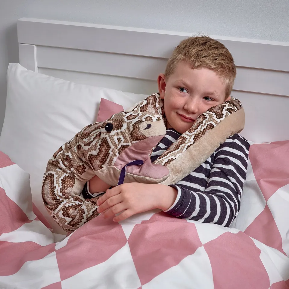 Boy hugs soft toy python on bed, ce marked for ages 18+ months.
