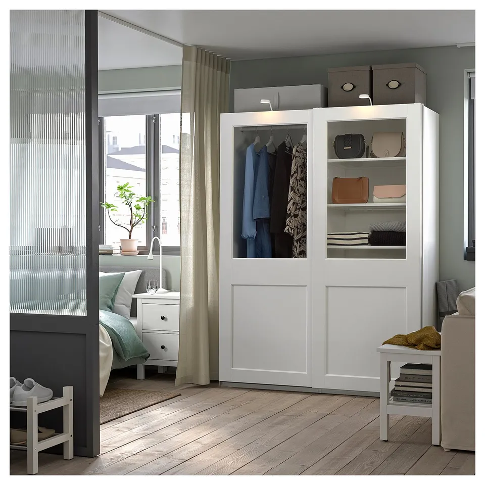A white PAX wardrobe with sliding glass doors, displaying clothes, and shelves with accessories.