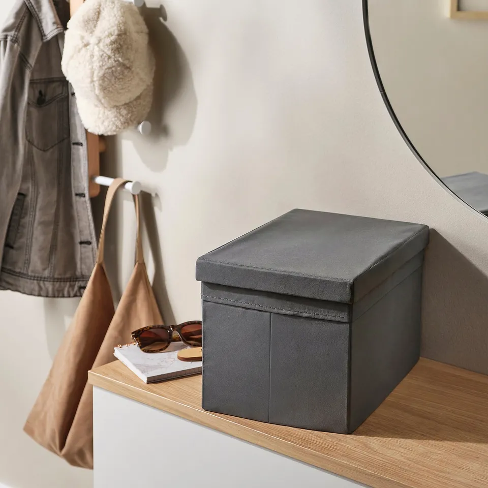 Grey box lid on shelf, with notebook and sunglasses. Coat and bag hang in background.