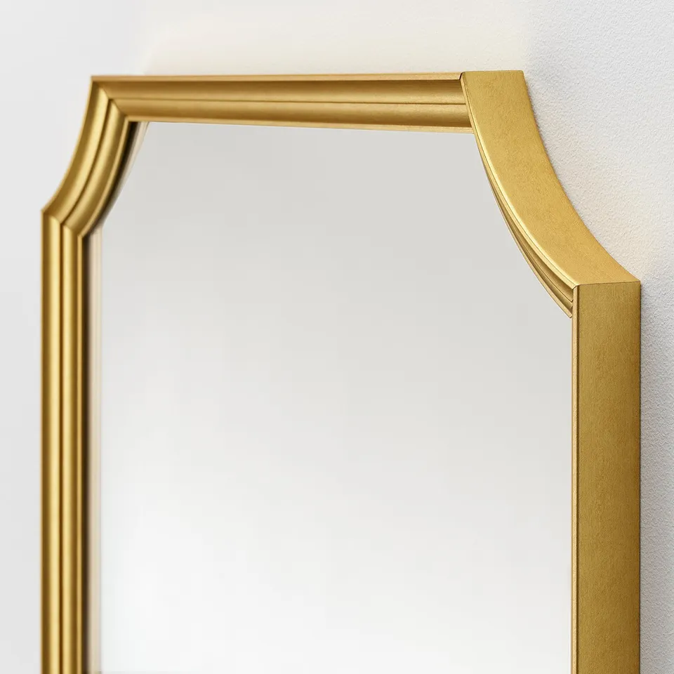 Gold-framed mirror with elegant design hangs vertically, reflecting a clean and pristine surface.