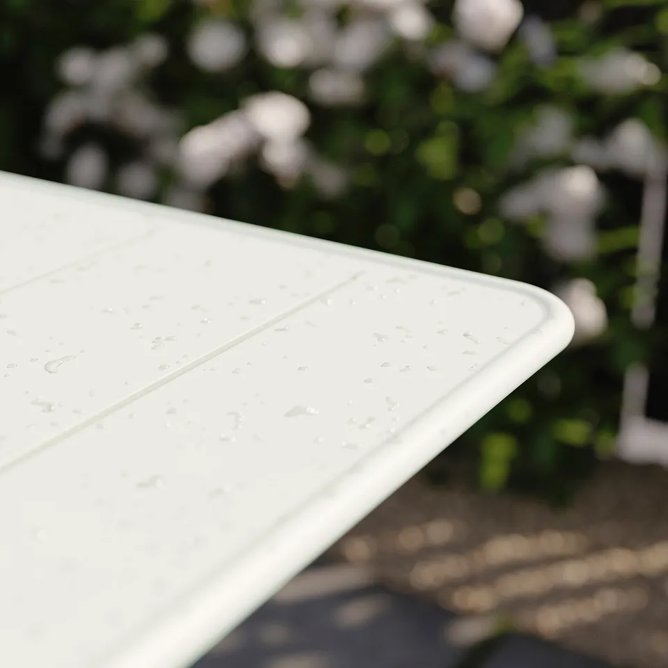 A corner of a white folded SUNDSÖ table. This durable, pre-assembled outdoor table is perfect for small spaces.