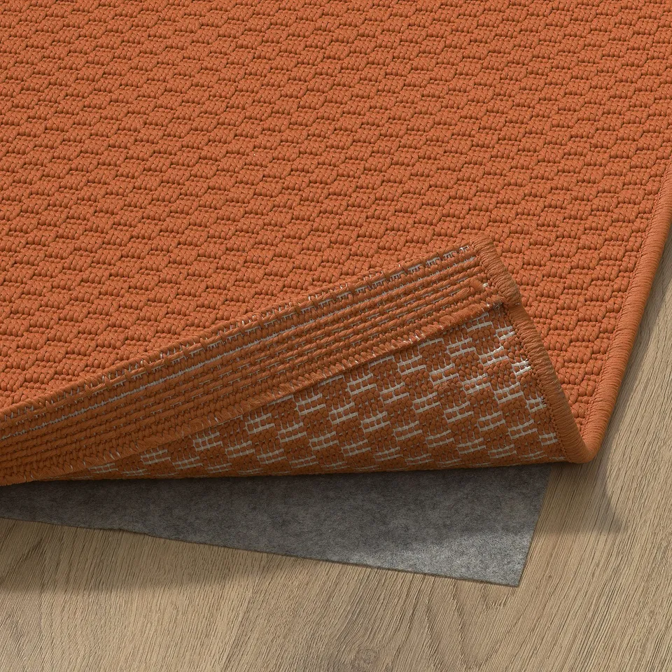 Orange textured rug on wooden floor, shown with anti-slip underlay.