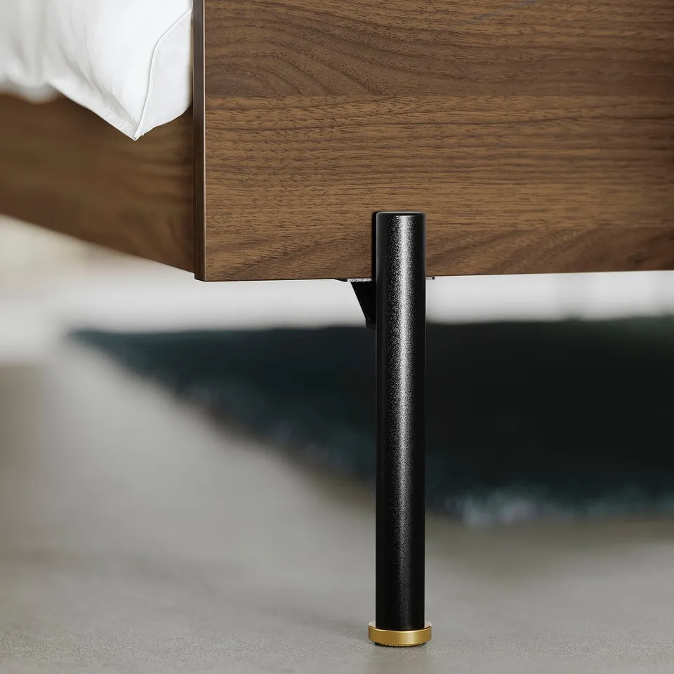 Close-up of a modern bed frame with sleek, black metal legs and gold accents, showcasing high-quality craftsmanship and contemporary design.