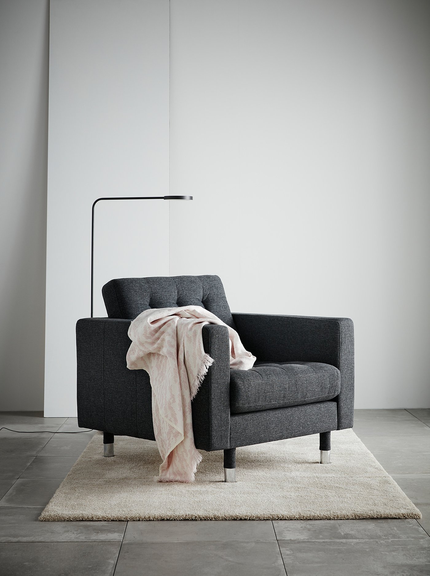 Modern dark grey armchair with light pink throw blanket and floor lamp.