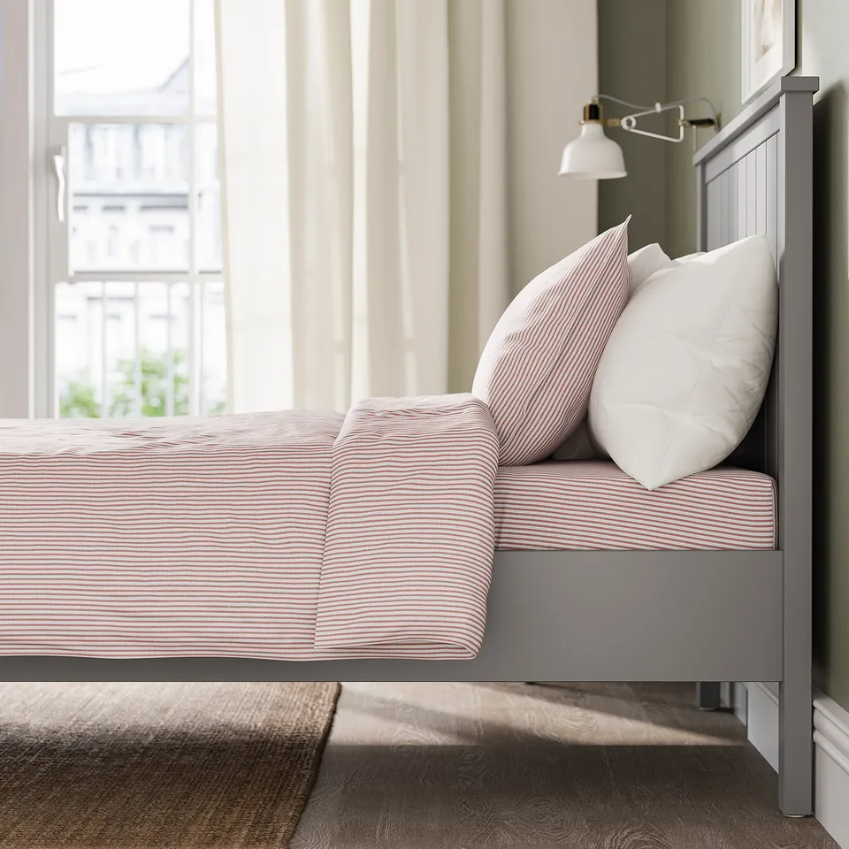 Grey bed, red striped pillows, storage, large window.