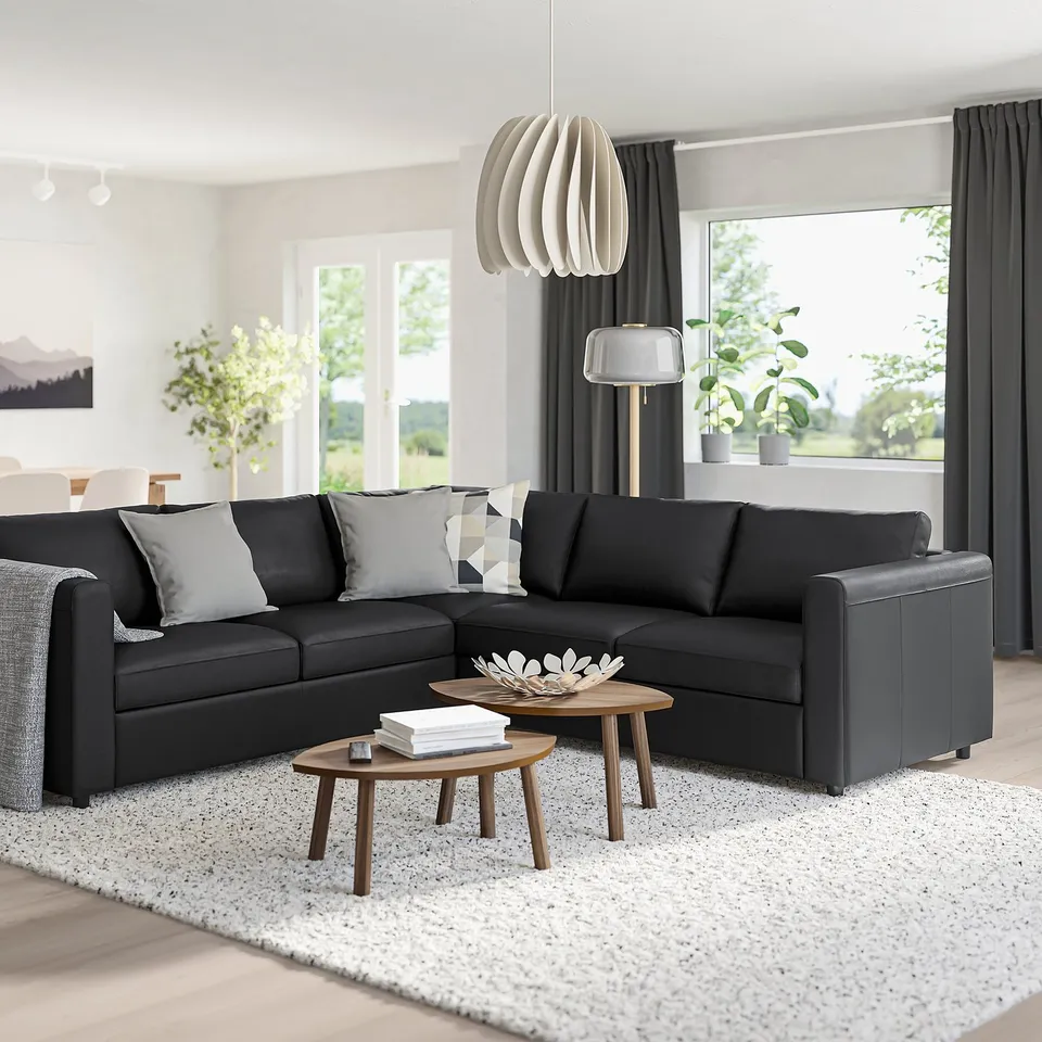 Modern living room with dark grey l-shaped VIMLE sofa, cushions, wooden coffee table, and white pendant light.