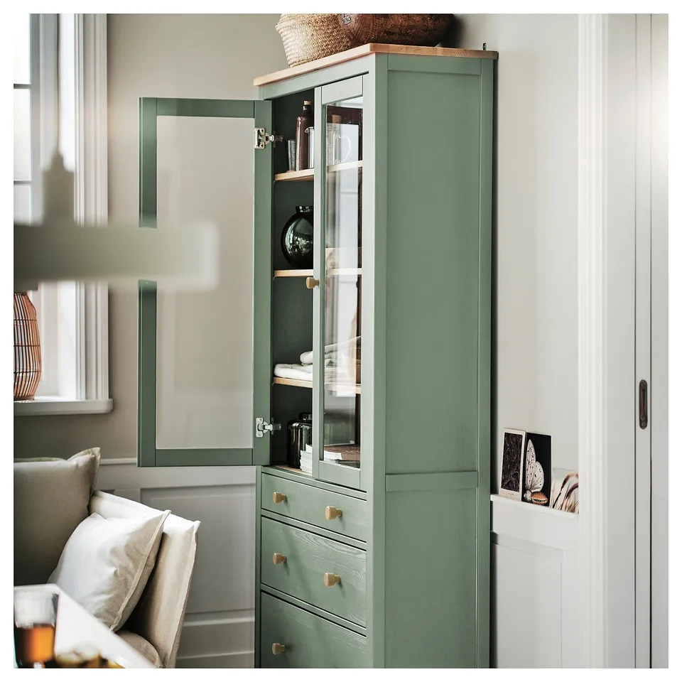 A green HEMNES glass-door cabinet with wooden drawers, displaying decorative items.