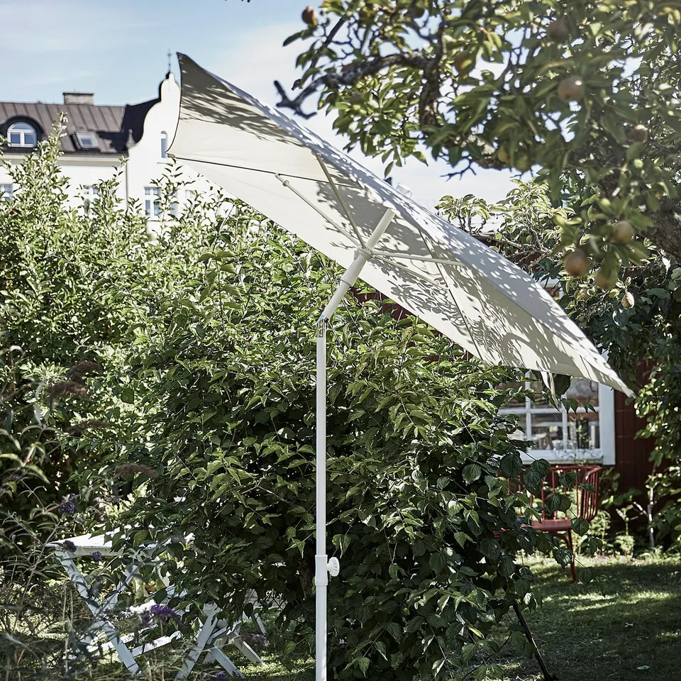 White TVETÖ parasol provides shade in a garden, tilted to block sun.