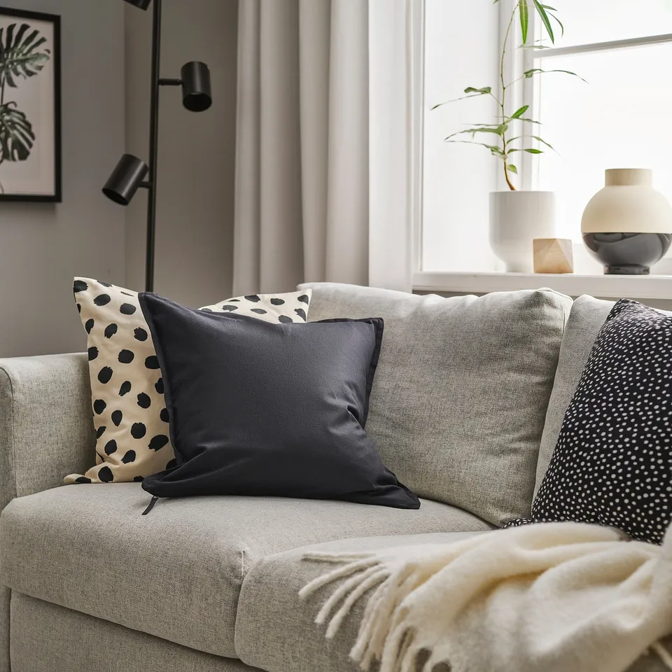 Sofa with cushions, black GURLI pillows, cream throw, vase, plant.