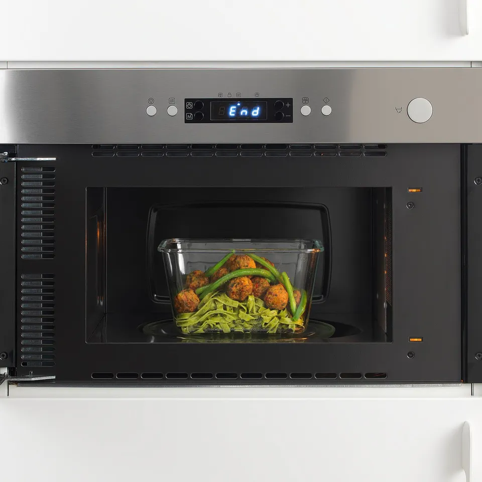 Stainless steel microwave with glass container inside, full of food. Digital display shows end at top.