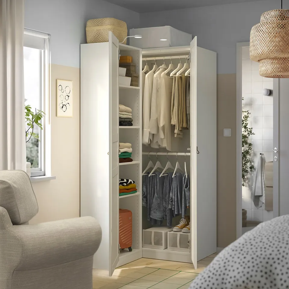 White wardrobe with clothes and baskets beside window and couch.