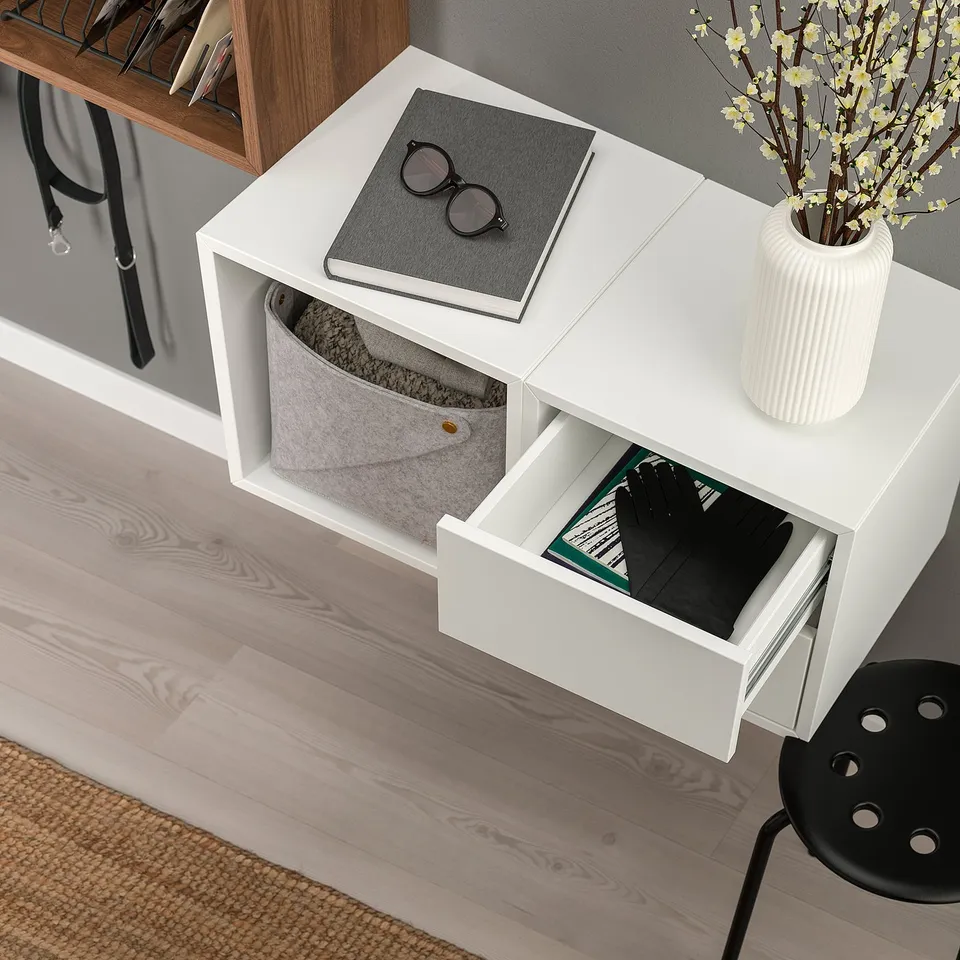 White wall-mounted storage unit with open shelf, drawer, and basket; displays books, stores items out of sight.